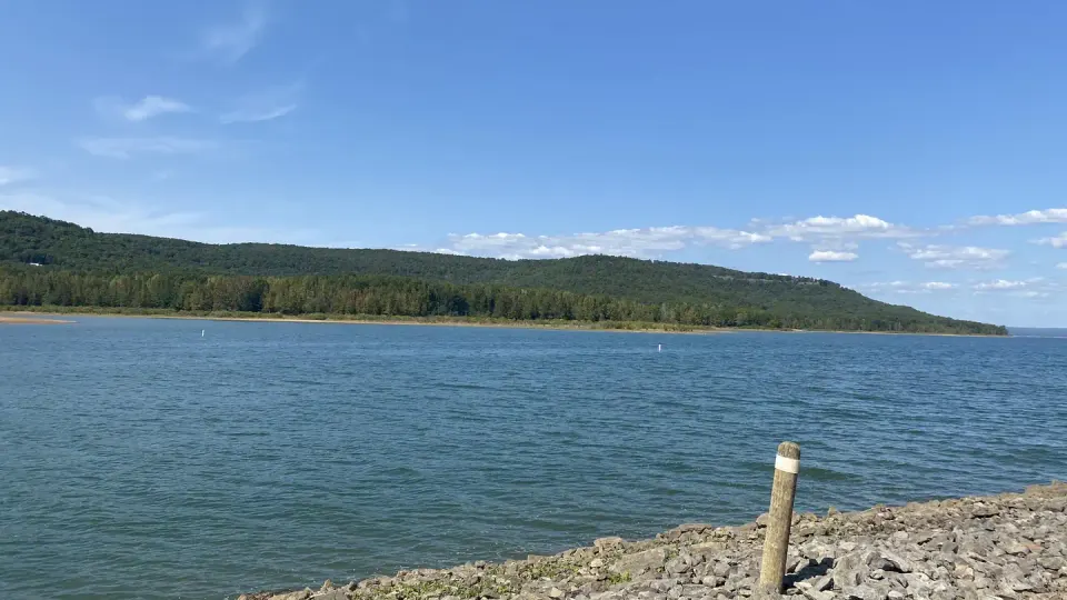 A rocky beach and a wide blue lake between low green hills