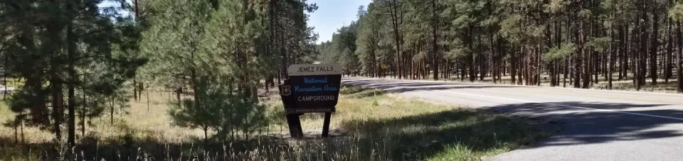 The entrance to Jemez Falls sign with pine forests in the background.