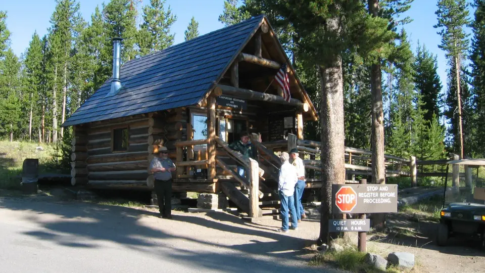 A park ranger and campground hosts in front of the rustic, log-structured Indian Creek Campground office.